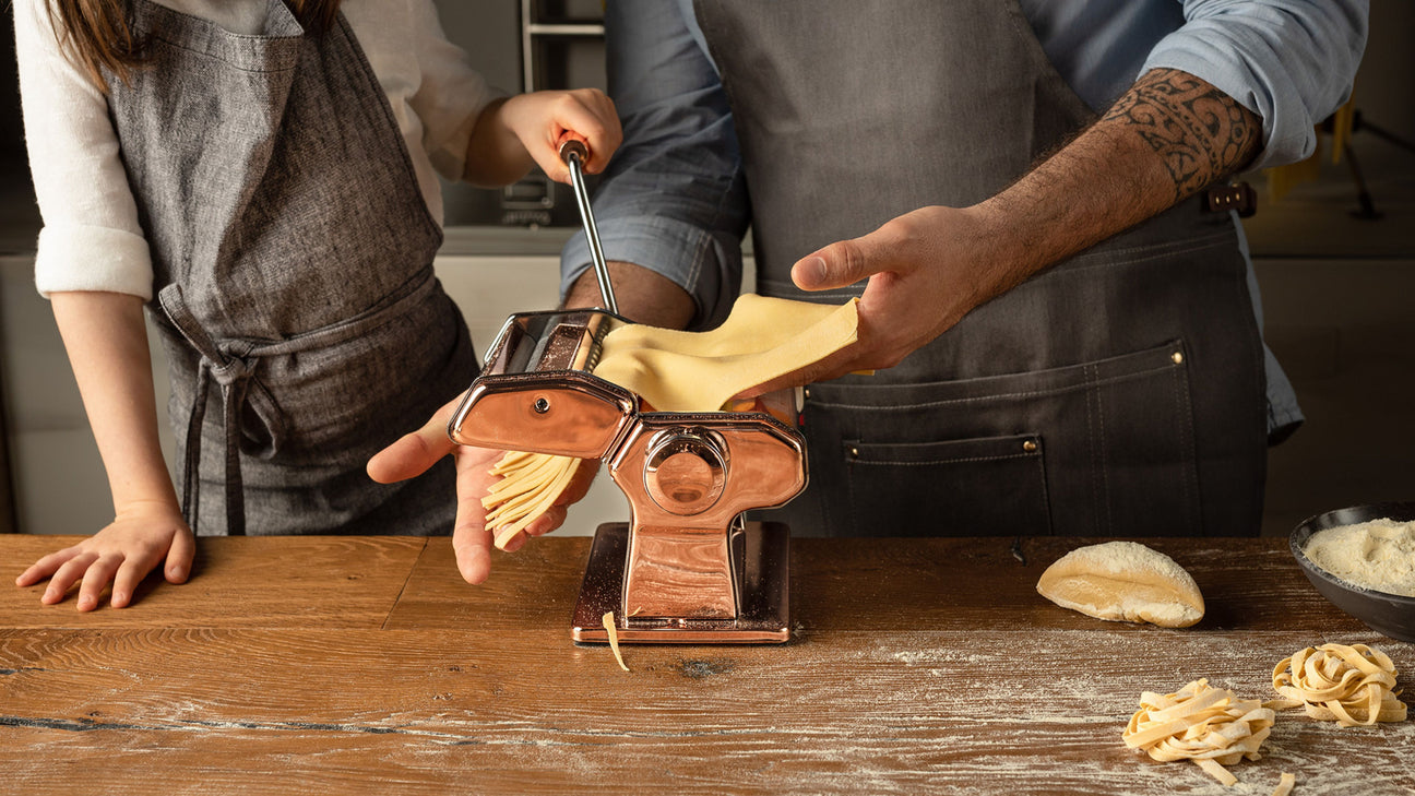 A couple using the Atlas 150 Pasta Machine to prepare pasta together in their kitchen.